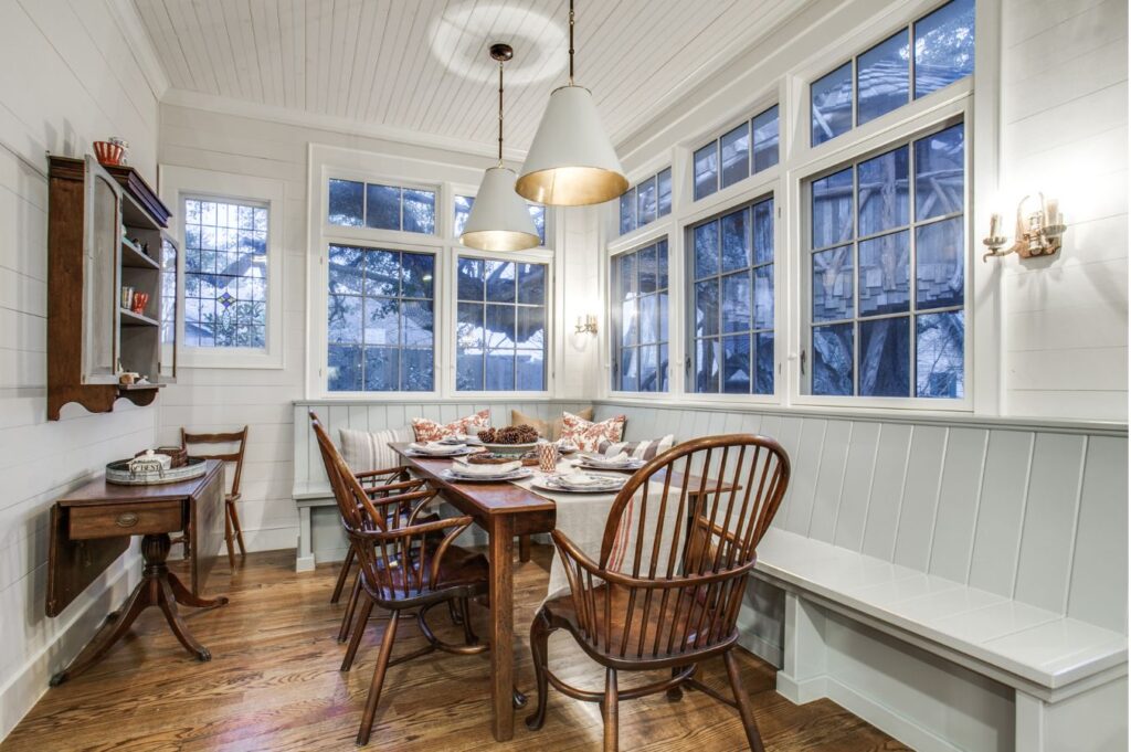 Cozy dining nook with a wooden table, spindle-back chairs, and bench, set for a meal. Large windows and warm lighting create an inviting space—styled by an expert interior designer Boerne TX for comfort and charm.