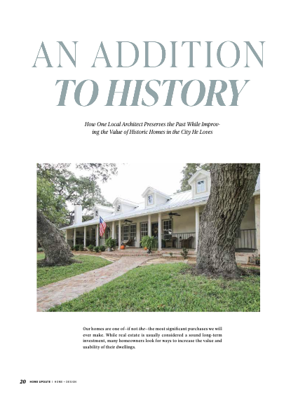 A large, historic, white house with a wraparound porch and American flag stands on a grassy lawn with mature trees, featured in a magazine article titled “An Addition to History” by an interior decorator Boerne expert.