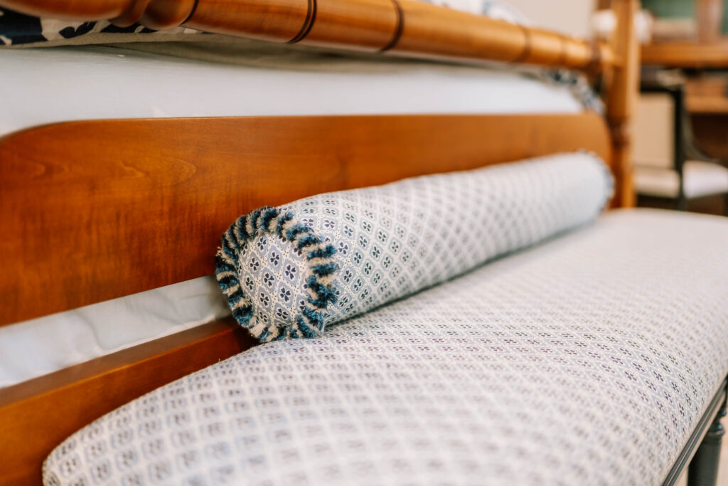 Close-up of a wooden daybed with a patterned bolster pillow and matching mattress in blue and white, showcasing fabric and wood textures—an inviting scene styled by an interior designer Boerne TX.