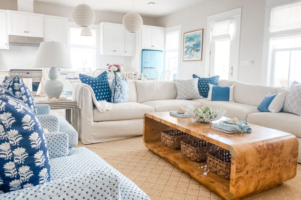 Bright, beach-style living room with a white sectional sofa, blue and white pillows, blue accent chairs, a wooden coffee table with woven baskets, and coastal decor. For similar airy spaces, consult an interior decorator Boerne trusts.