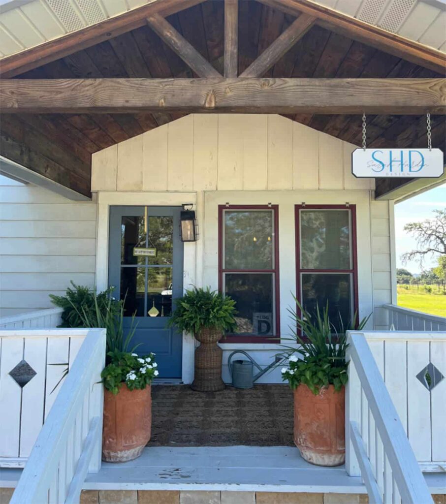 The Bungalow studio entrance: a covered porch with exposed timber beams, a blue front door and a hanging SHD Design sign