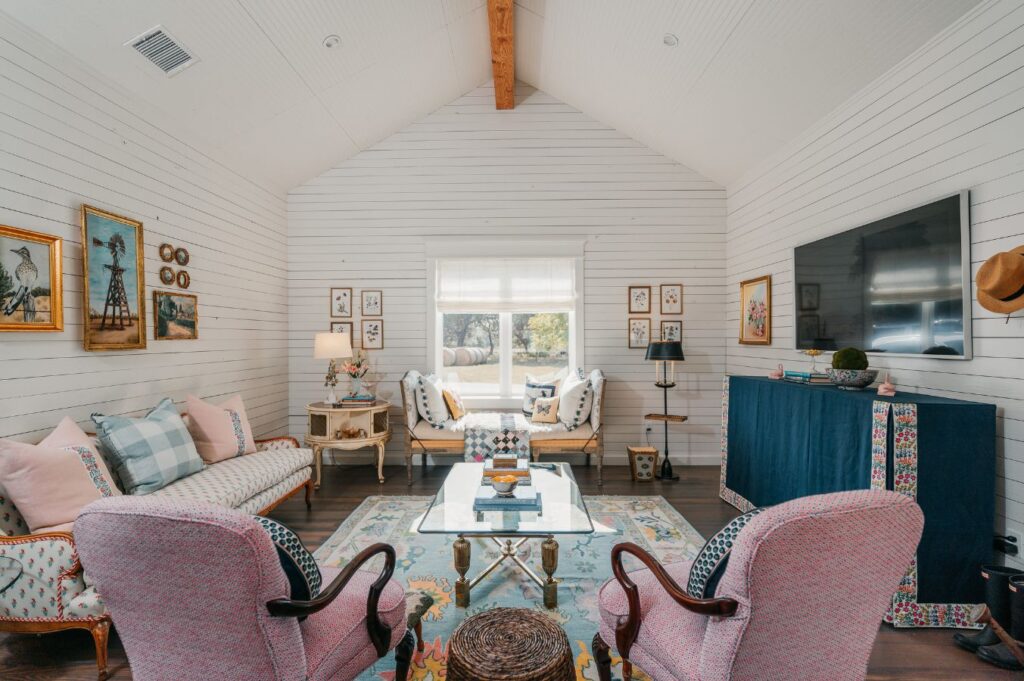 A cozy, eclectic living room with white shiplap walls, colorful patterned furniture, and a blue cabinet by the window, expertly styled by an interior design company in Boerne, TX. Natural light fills the space.