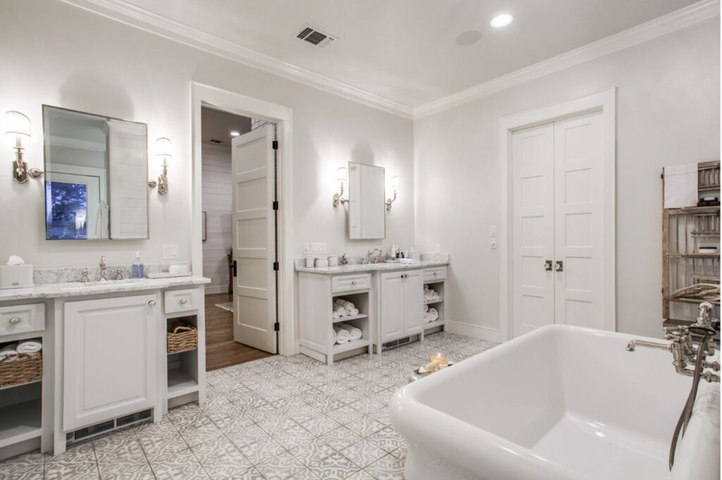 Elegant bathroom with patterned tile floor, white freestanding bathtub, dual vanities, and open shelving. Designed by an expert interior designer Boerne TX, the space features neutral tones, bright lighting, and stylish details throughout.