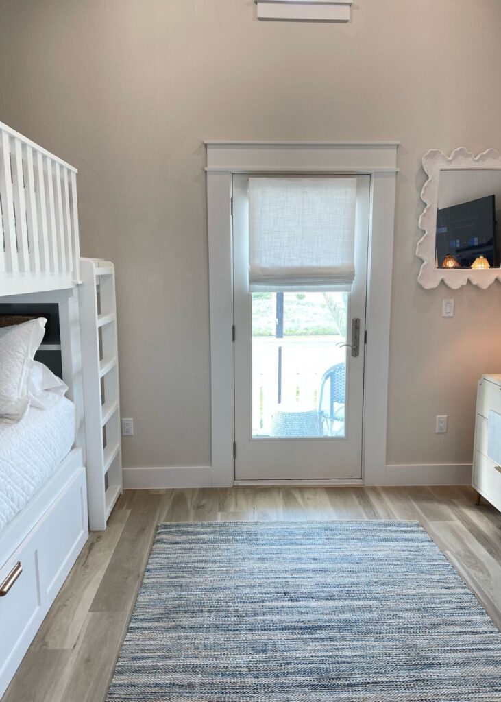 A bright bedroom with wood flooring, a blue-striped rug, bunk beds on the left, and a dresser with a mirror on the right—perfect inspiration from an interior designer Boerne TX for your next home update.