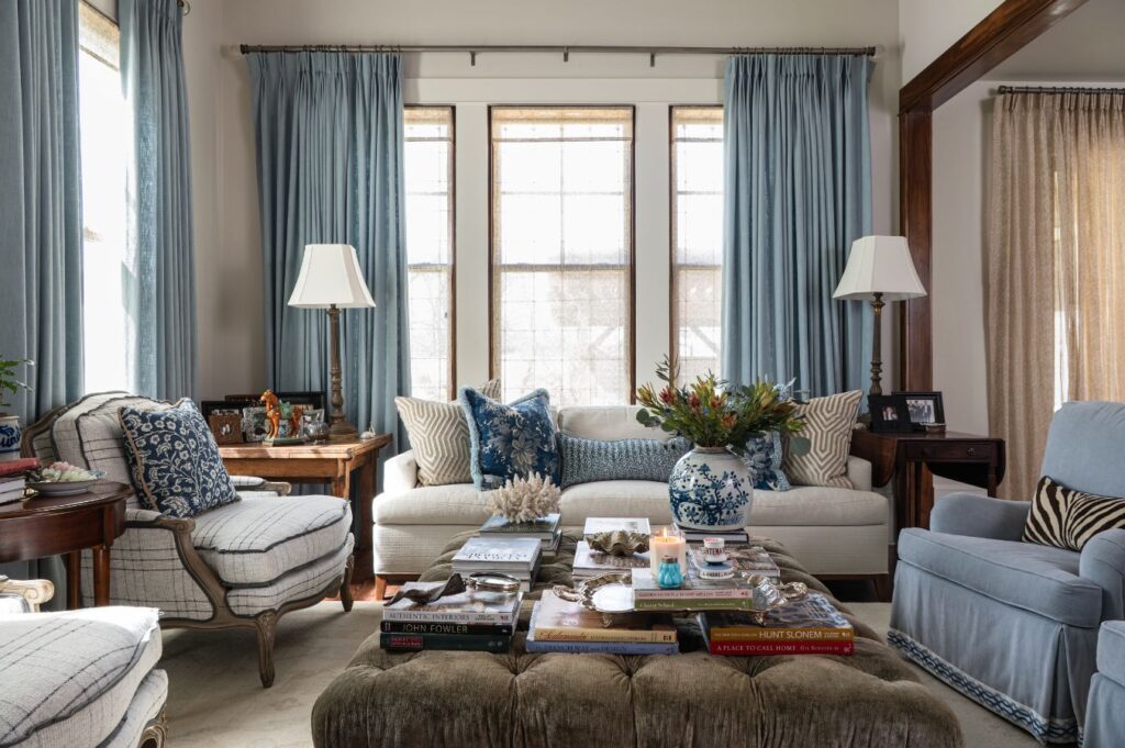 Elegant living room with blue curtains, a white sofa, patterned pillows, and a blue chair. Styled by an interior designer Boerne TX, the space features tasteful decor, cozy armchairs, and side tables with lamps for a welcoming ambiance.
